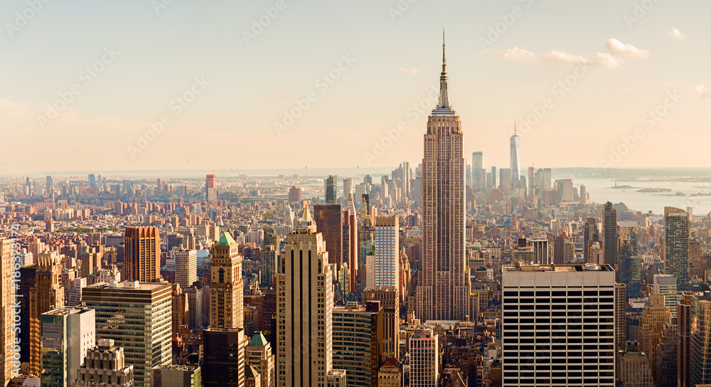 Panorama Nowego Jorku z widokiem na Empire State Building na pierwszym planie. W tle widoczne są wieżowce Dolnego Manhattanu, w tym One World Trade Center, oraz delikatne odcienie zachodzącego słońca.