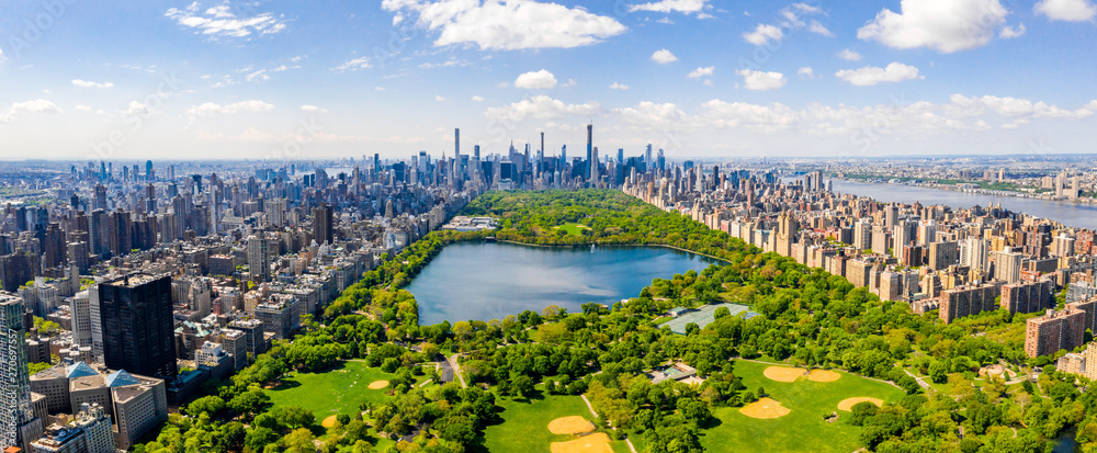 Panorama Central Parku w Nowym Jorku z lotu ptaka. Widok obejmuje zielone tereny parku otoczone wieżowcami Manhattanu, z charakterystycznym skyline Midtown i Upper West Side. Na pierwszym planie widoczne są jezioro oraz boiska.