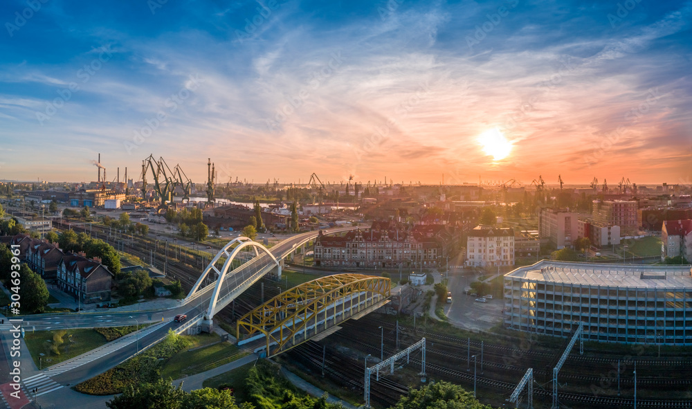 Gdańsk, wiadukty, stocznia w tle, dźwigi, wschód słońca, industrialny krajobraz.