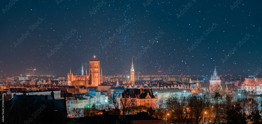 Gdańsk nocą, panorama miasta, Bazylika Mariacka, gwieździste niebo, oświetlone budynki.