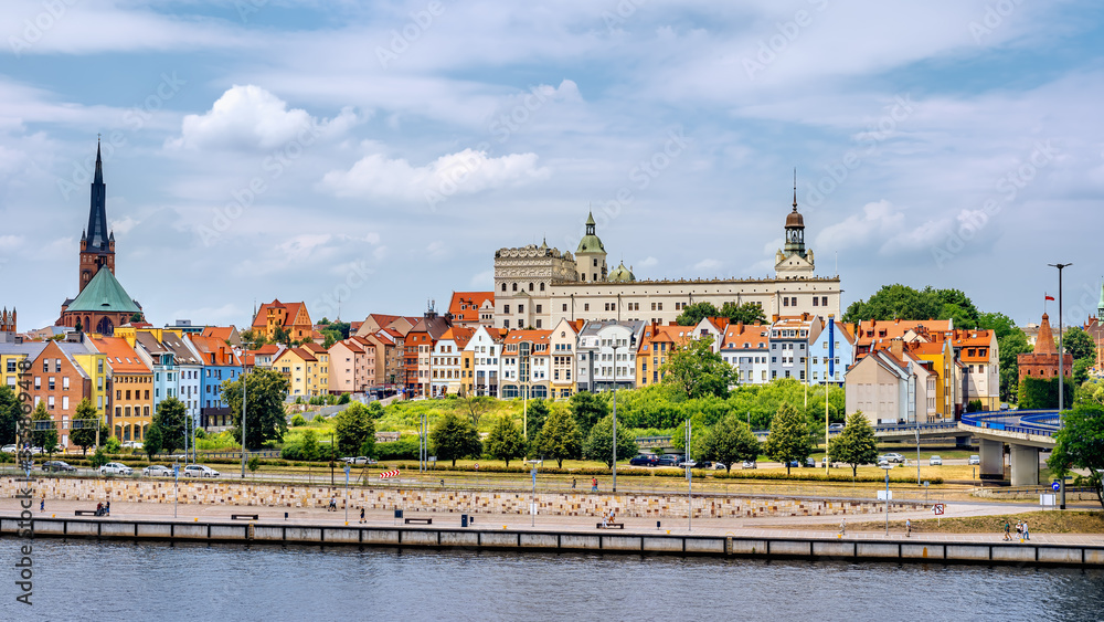 Panorama nabrzeża Szczecina - kolorowe kamienice tworzą malowniczy pejzaż na tle Zamku Książąt Pomorskich i kościelnej wieży, letnie niebo i spokojna woda Odry podkreślają urok portowego miasta