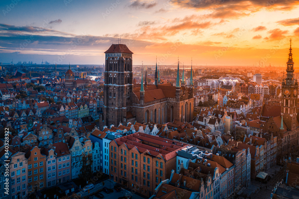 Bazylika Mariacka w Gdańsku o zachodzie słońca - monumentalna gotycka świątynia z charakterystyczną wieżą dominuje nad mozaiką kolorowych kamienic, których fasady lśnią w ciepłym świetle zachodzącego słońca