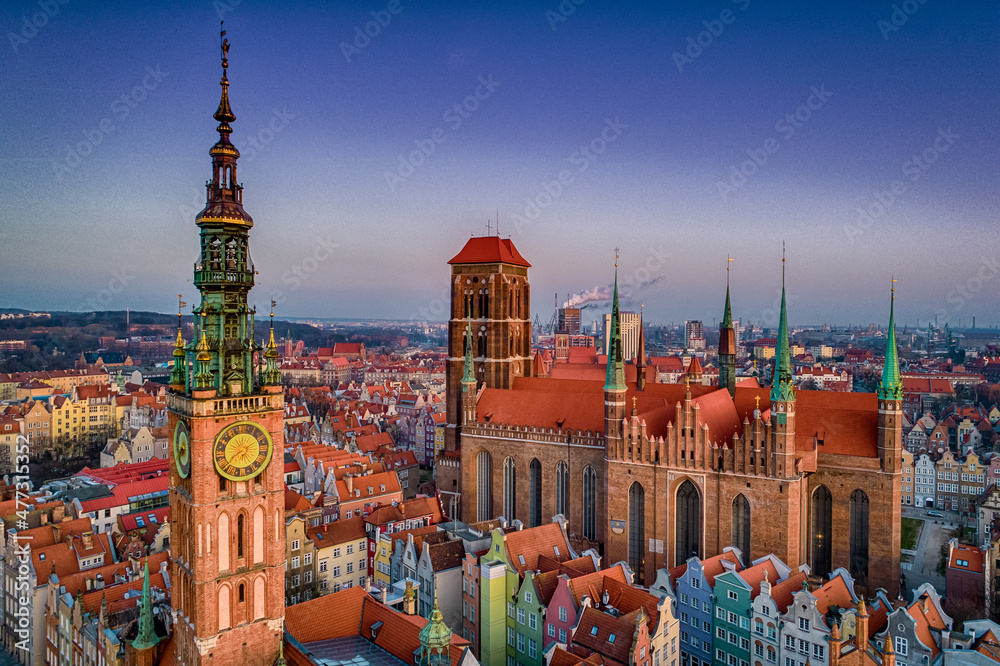 Panorama historycznego Gdańska w ciepłym świetle - monumentalny Ratusz Głównego Miasta ze złotą wieżą dominuje nad mozaiką kolorowych kamieniczek i majestatyczną Bazyliką Mariacką, których wieże wznoszą się ku fioletowemu niebu