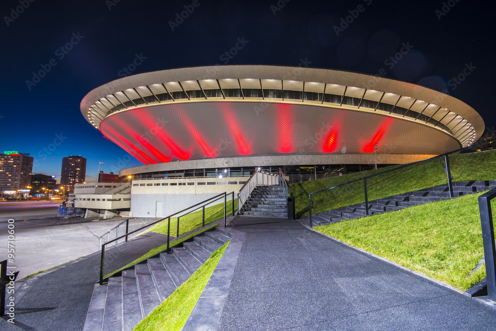 Spodek w Katowicach nocą, podświetlony na czerwono, z widokiem na schody prowadzące do wejścia. Nocna architektura miejska, Katowice, Polska.